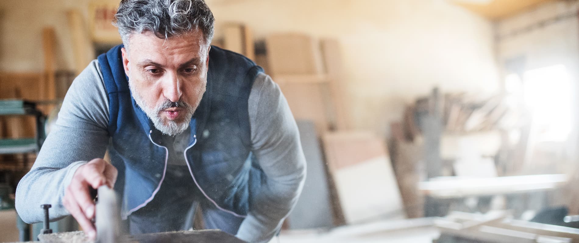 A mature man worker in the carpentry workshop, working with wood.